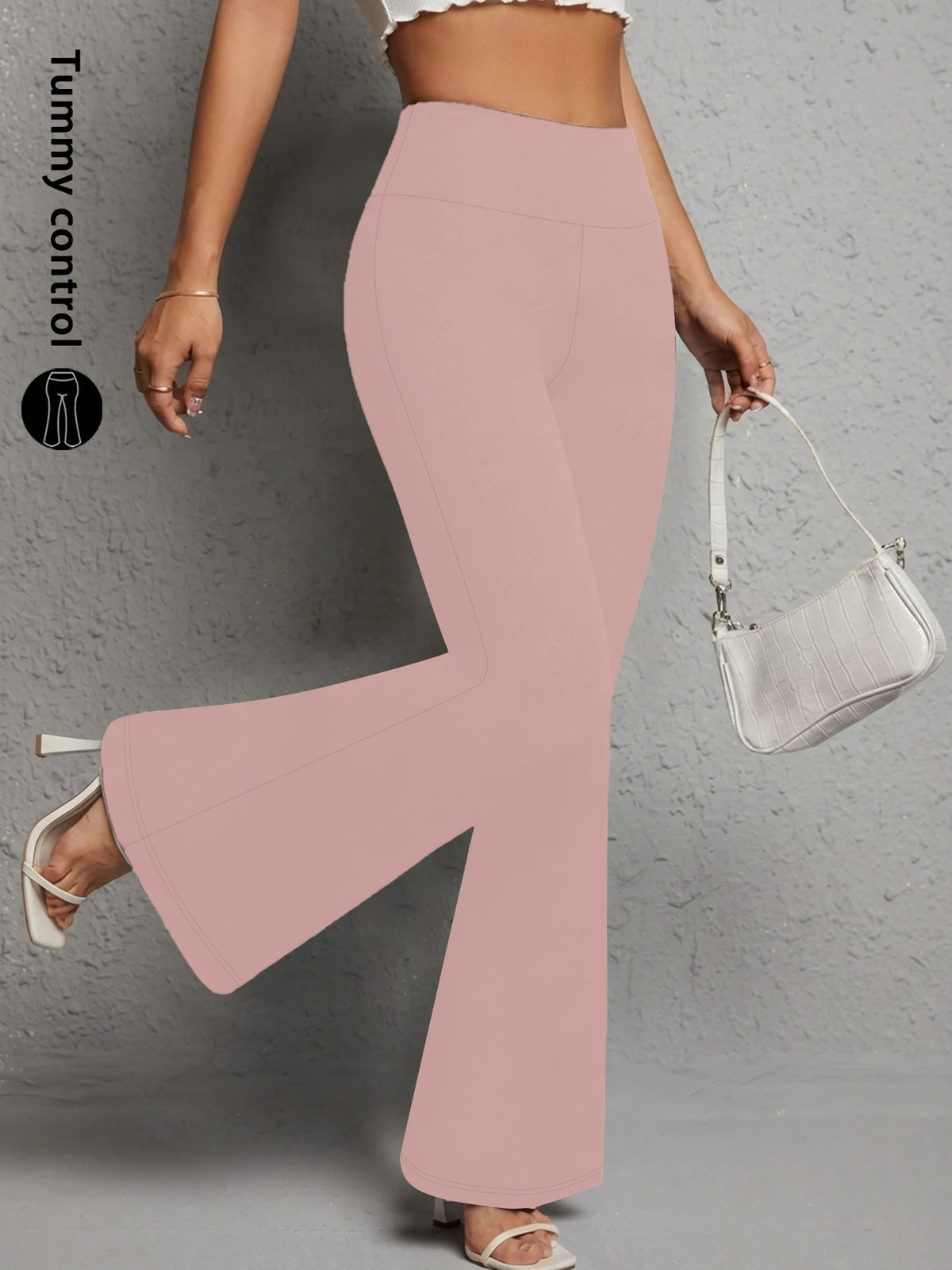 A model wearing light pink flared yoga trousers and a white shoulder bag.