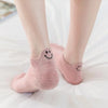 A pair of pink knitted ankle socks with embroidered smiling faces lying on a white surface.