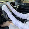 A person wearing long white sleeves is holding a steering wheel inside a car, demonstrating UV protection arm sleeves.
