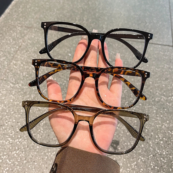 A hand holds a stack of three classic square frame eyeglasses with tortoiseshell and olive green frames.