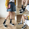 A person models black and white athletic shoes and black socks, wearing a yellow jacket and denim shorts.