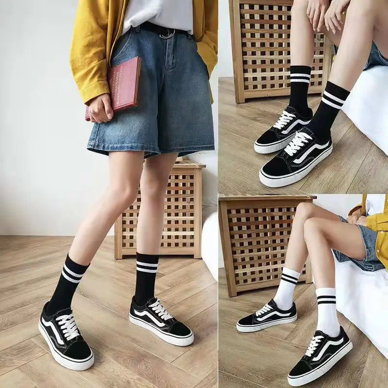 A person models black and white athletic shoes and black socks, wearing a yellow jacket and denim shorts.