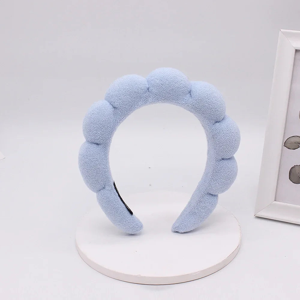 Light blue sponge terry cloth headband for hair styling displayed on a white stand.