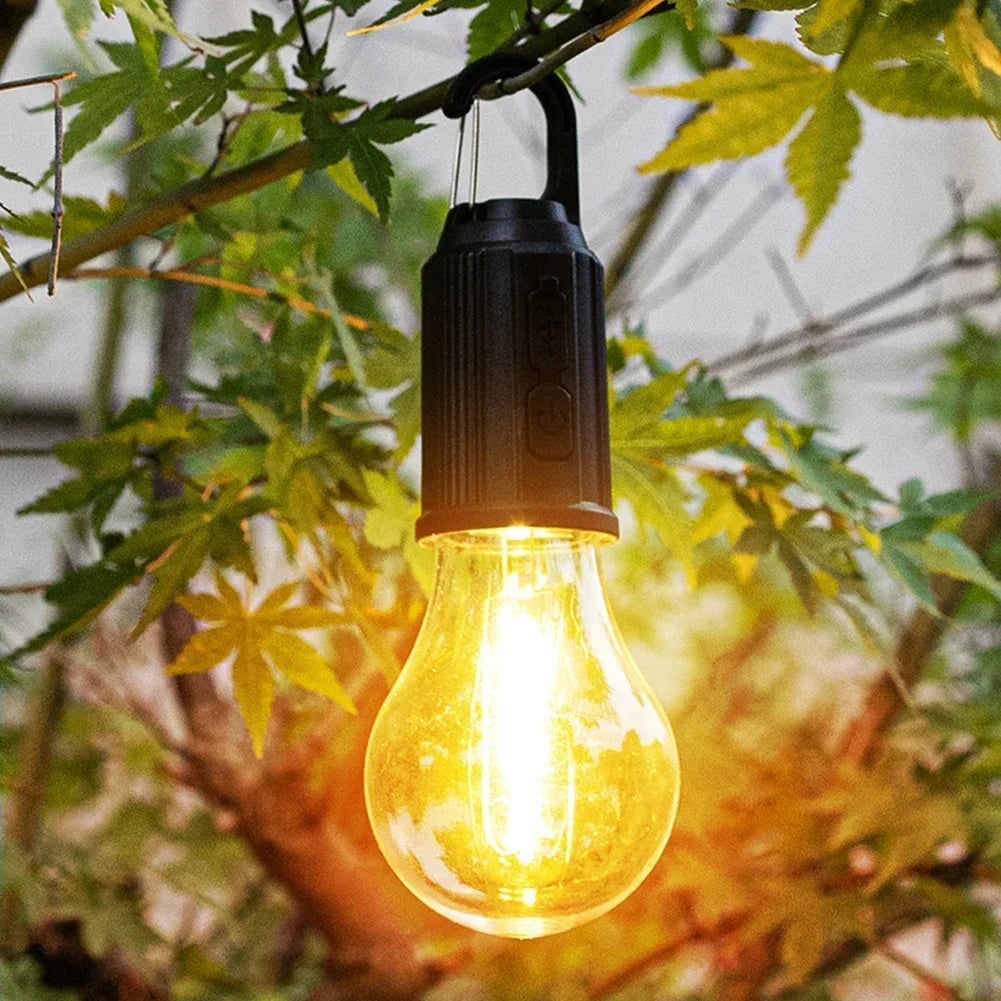 A yellow light bulb lantern hangs from a branch amidst green leaves.
