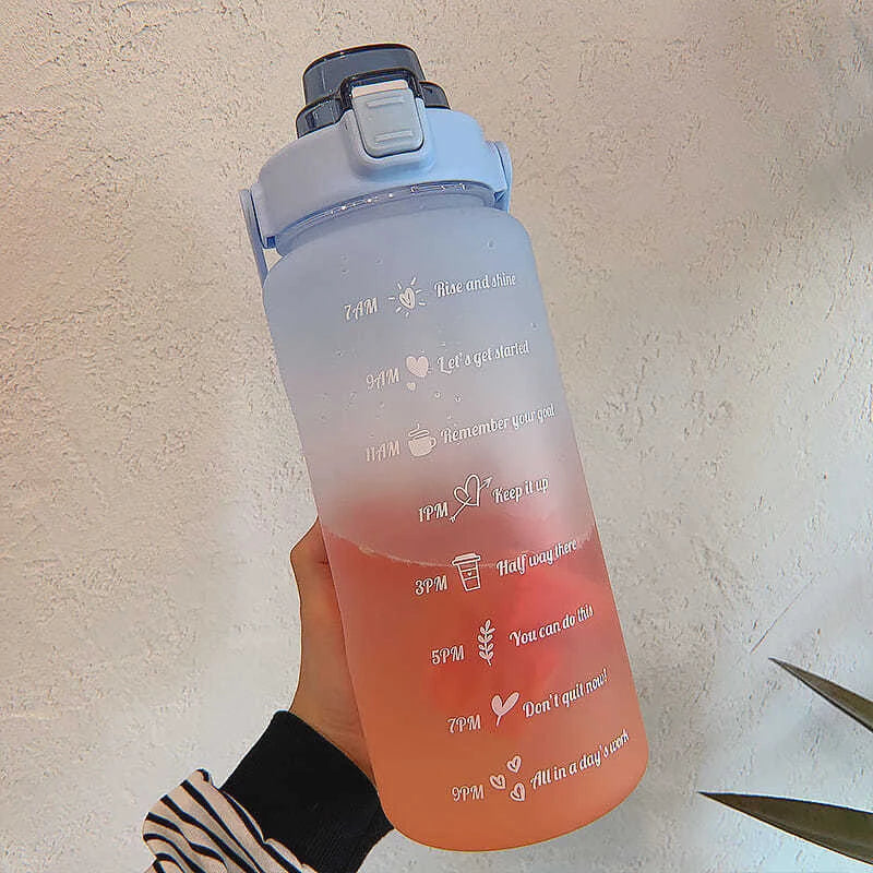 Una mano sostiene una botella de agua transparente rosa con texto motivacional sobre un fondo claro.