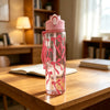 A clear water bottle with a pink lid and pink strawberry bow design sits on a wooden table.