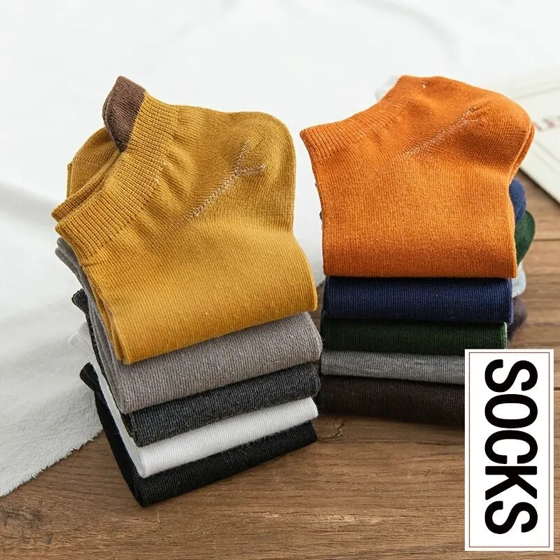 Stapel Herrensocken aus Baumwolle in erdigen und neutralen Tönen wie Senffarben, Orange, Grau und Schwarz.