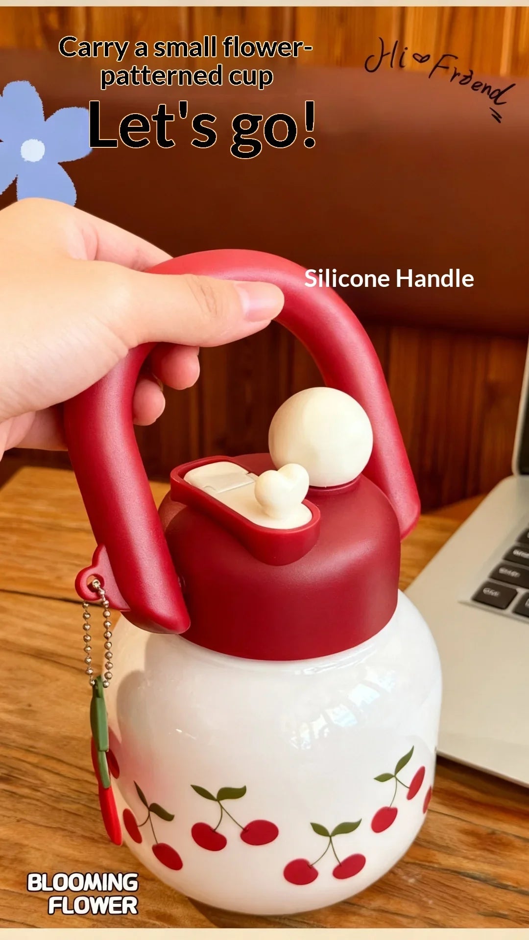 Una taza de silicona con estampado de flor roja y blanca y asa, sostenida junto a una botella blanca.