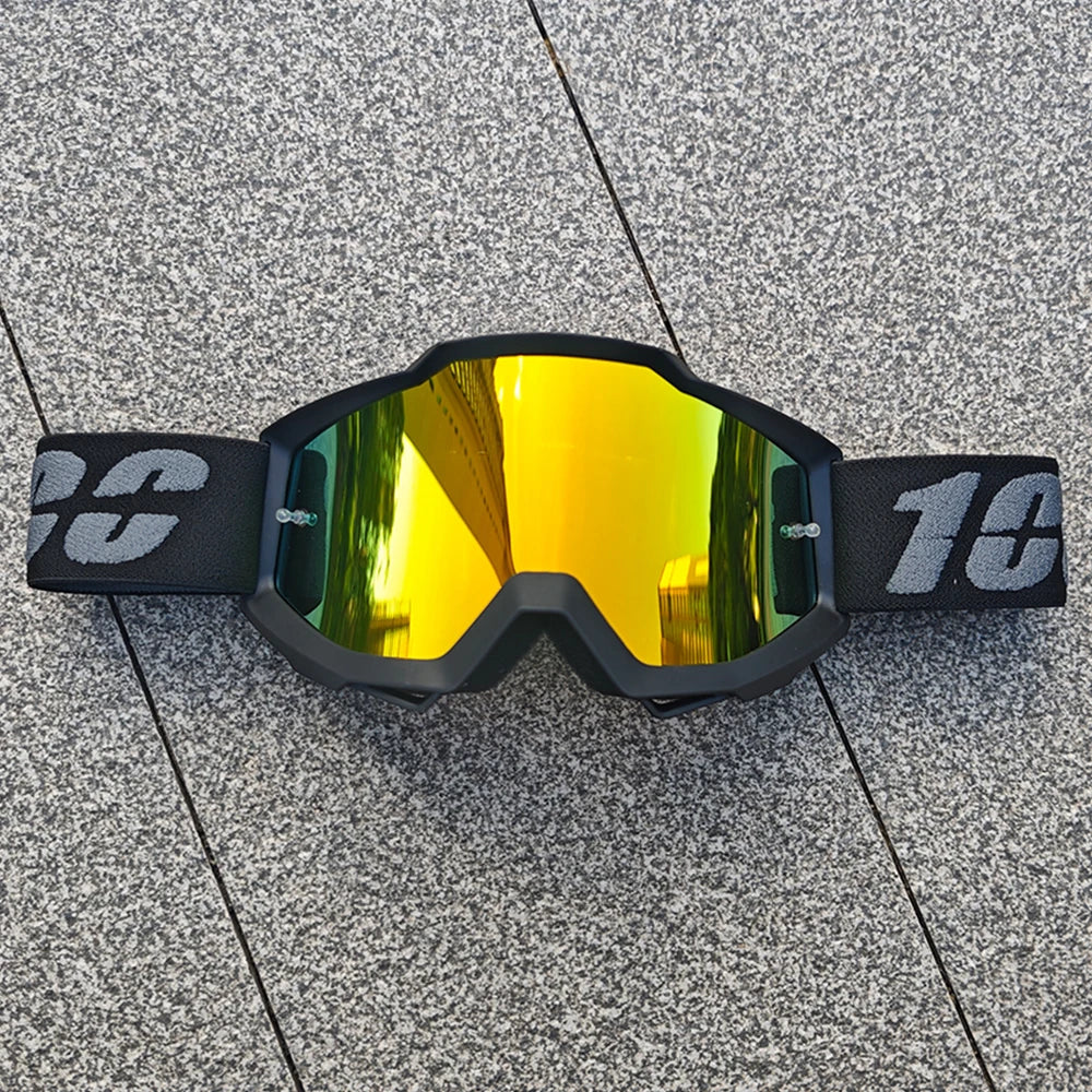 Une paire de lunettes tout-terrain noires avec des verres teintés jaune reposant sur une surface grise texturée.