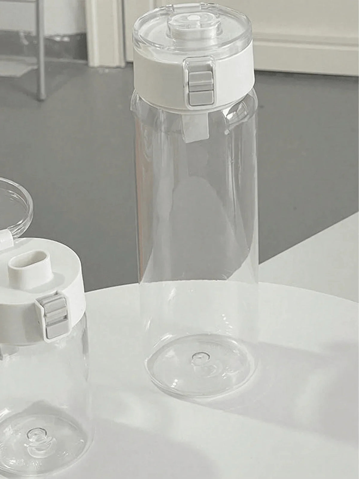 A clear sports water bottle with a white cap is shown on a white surface.