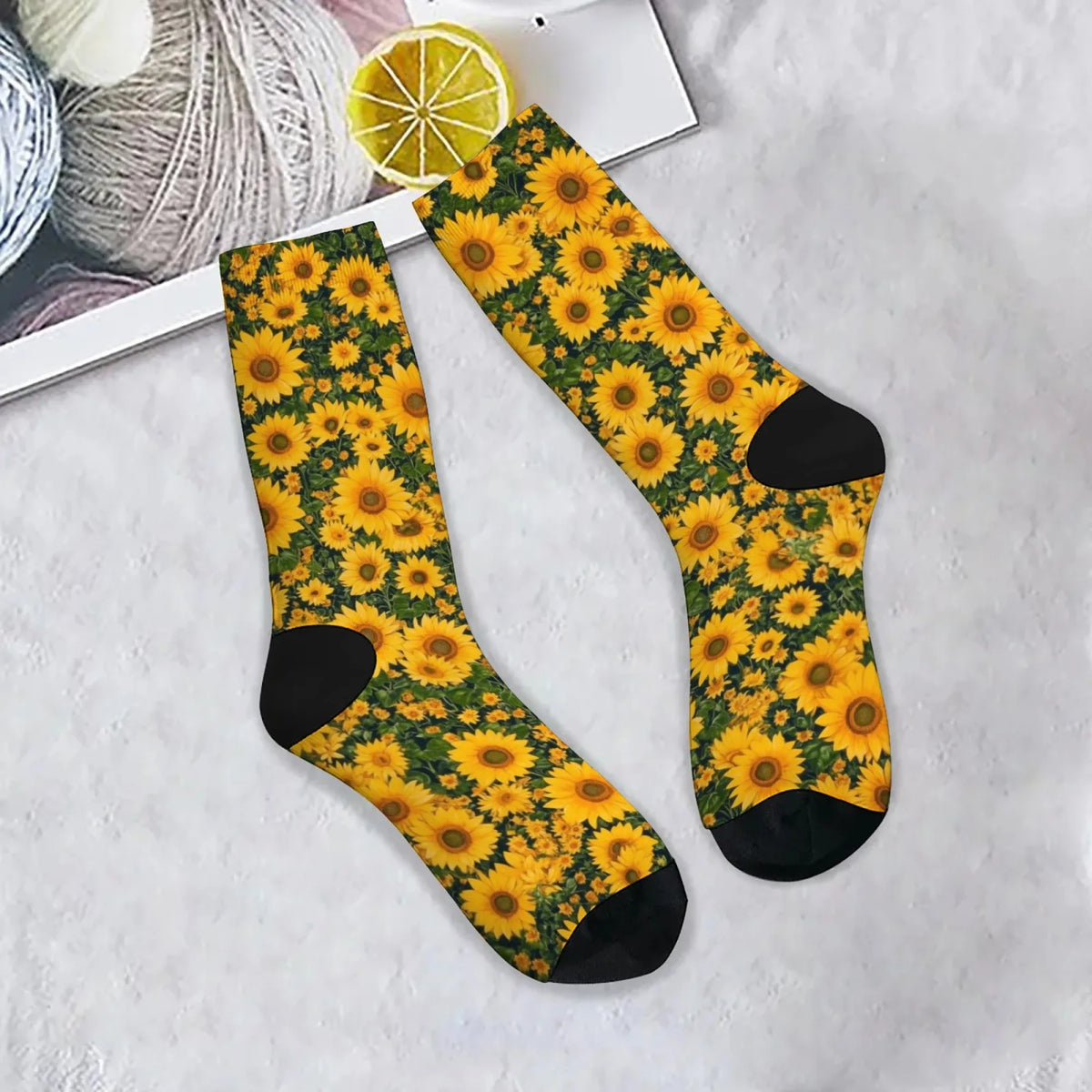 A pair of yellow and green sunflower print breathable crew socks lying on a white surface next to a slice of lemon.