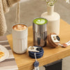 A stainless steel insulated thermos bottle next to a white ceramic mug and a glass vase on a wooden table.