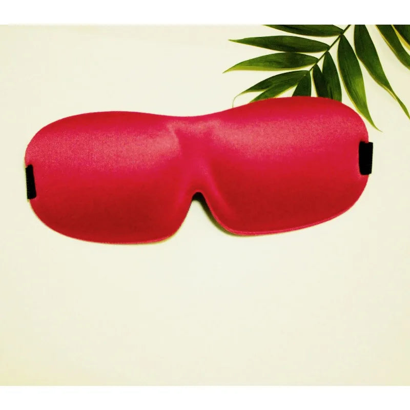 A bright red memory foam sleep mask lying on a light background with green leaves in the background.