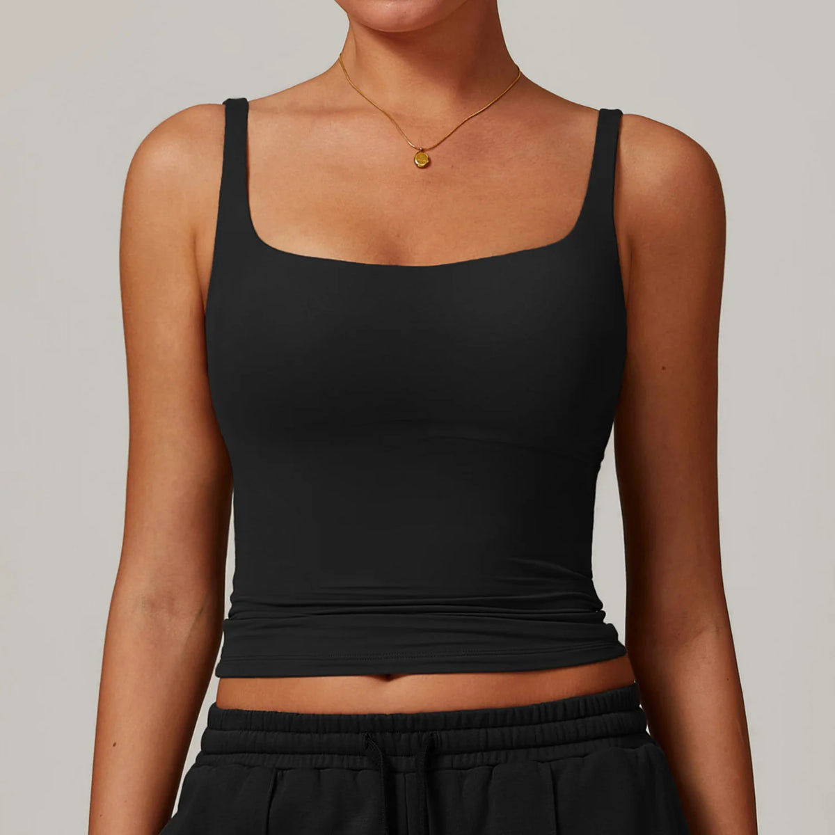 Una mujer vistiendo un top deportivo de cuello cuadrado negro y pantalones deportivos negros.