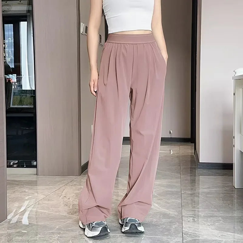 A woman wearing loose mauve yoga pants and a white top standing indoors.