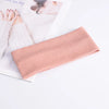 A pink ribbed knitted headband is displayed next to a book and hands.