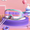Pink and teal swimming goggles resting on a purple stack, with a pink background and a light blue tree in the background.