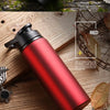 A red and black leakproof aluminum portable water bottle resting on a wooden surface with natural elements.