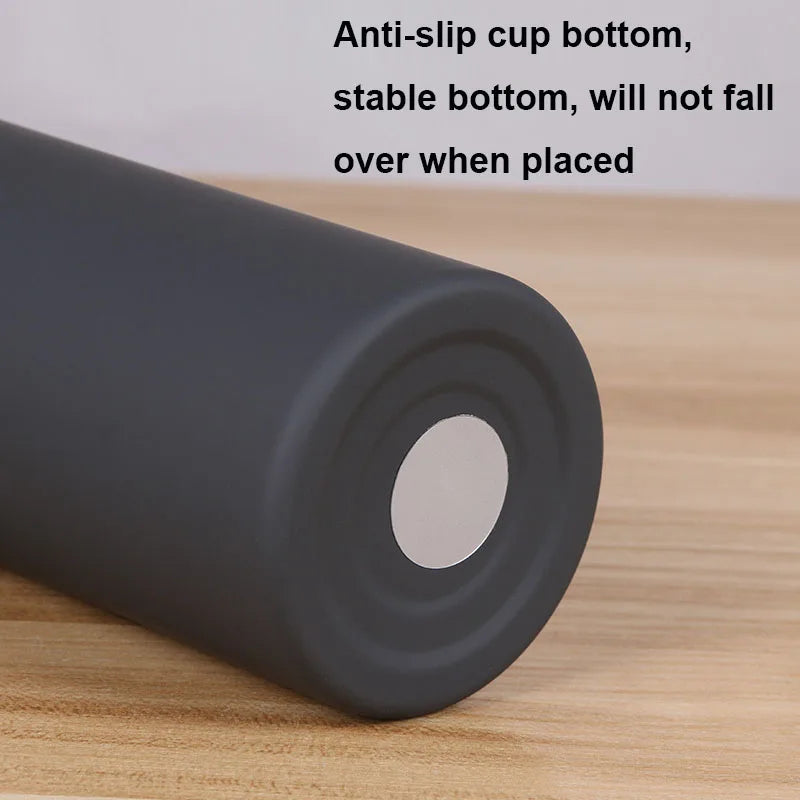 A dark gray double-layer vacuum thermos cup with an anti-slip bottom resting on a wooden surface.