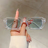 A hand holds a pair of clear plastic rectangle sunglasses against a light background.