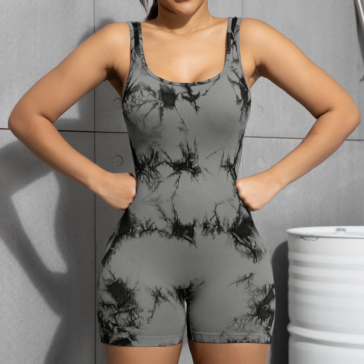 A model wearing a gray tie-dye sport jumpsuit, posing against a gray wall.