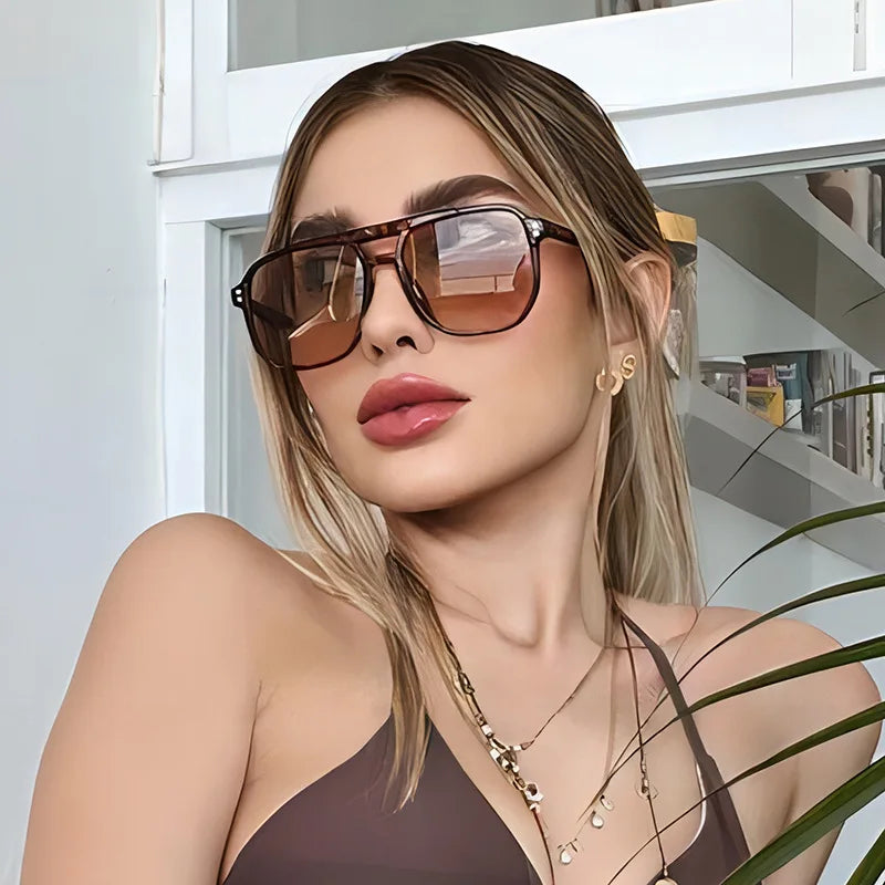 A woman wearing vintage square sunglasses with a double bridge and a delicate gold necklace.