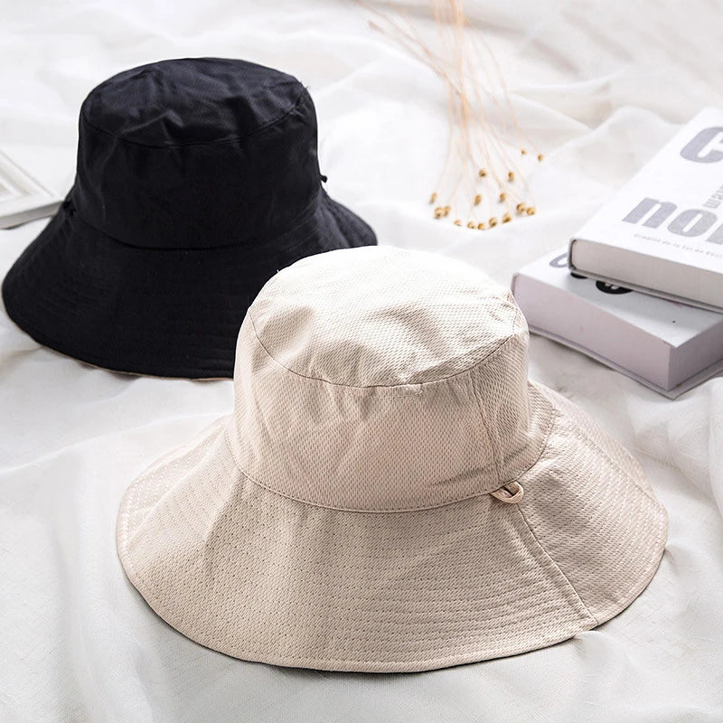 A beige double-sided wide brim bucket hat is displayed on a white fabric surface.