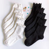 A stack of white cotton ruffle ankle socks and black ankle socks are displayed on a white background.