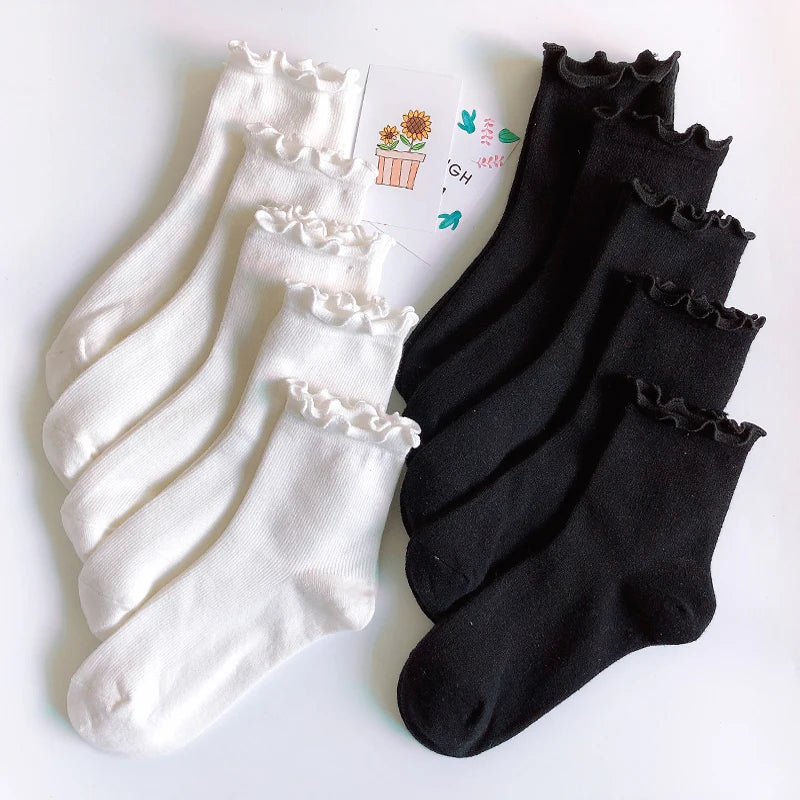 A stack of white cotton ruffle ankle socks and black ankle socks are displayed on a white background.