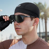 A man wearing a black cycling cap and dark sunglasses outdoors.