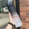 A hand holds a gradient insulated sports water bottle with a black cap against a brick wall backdrop.