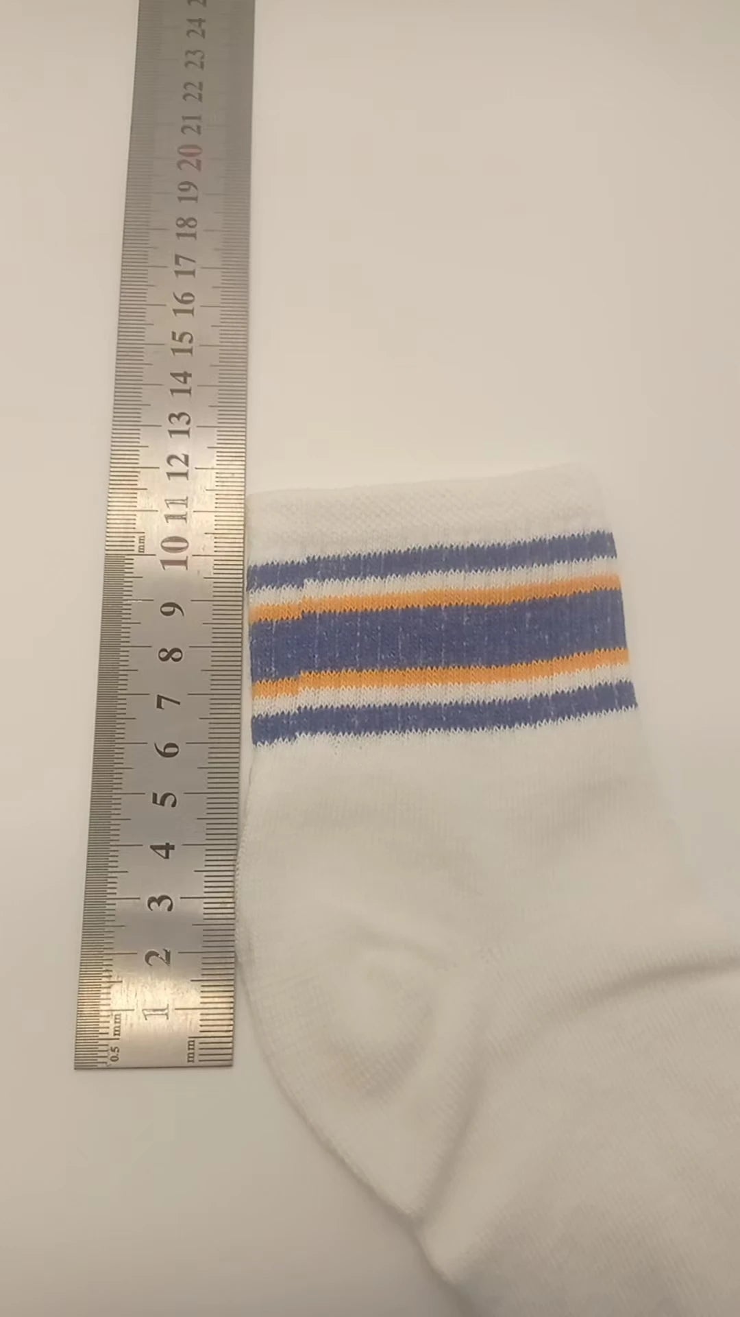 White casual socks with blue, orange, and gray horizontal stripes shown next to a ruler.