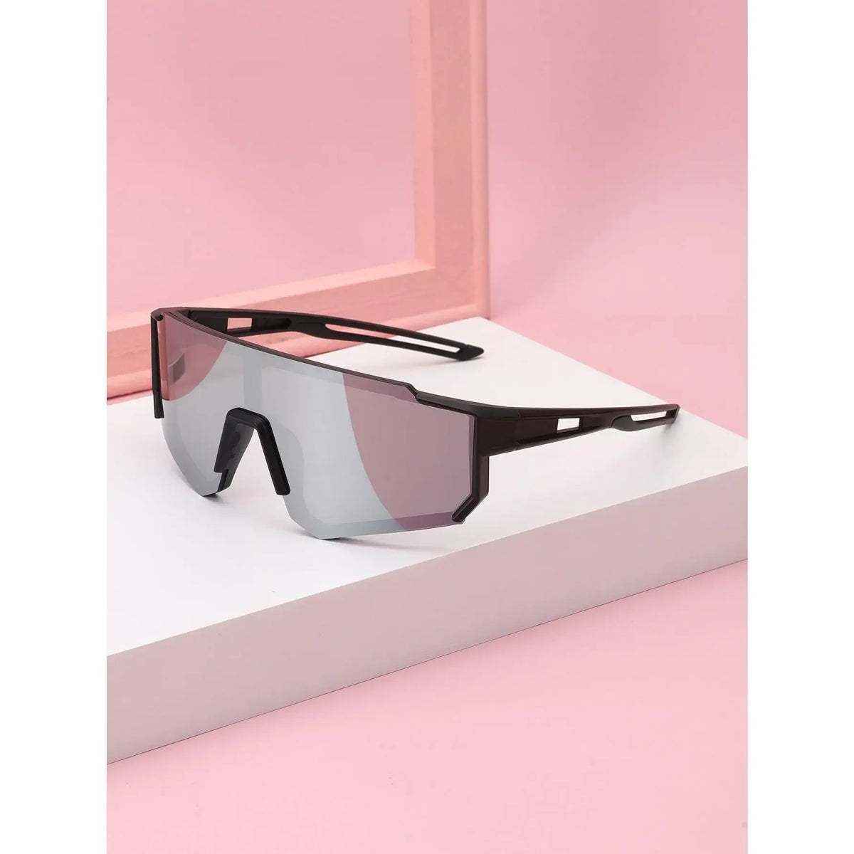 A pair of dark gray sports sunglasses with black frames resting on a white surface against a pink background.