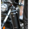 A black insulated stainless steel thermal water bottle is being held by a gloved hand in an outdoor setting.