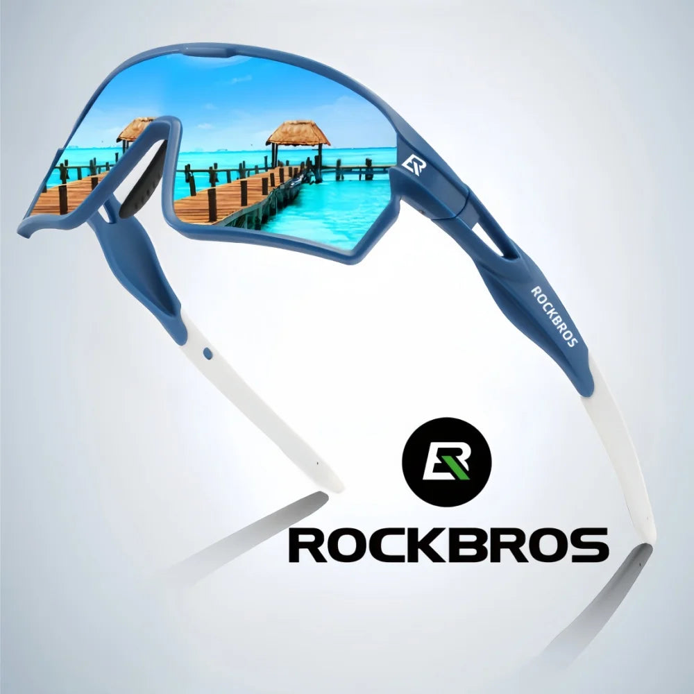 A pair of blue polarized cycling sunglasses with white arms and a Rockbros logo, set against a tropical sea background.
