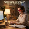 A woman wearing red lens eye protection glasses works at a desk with a laptop and lamp.