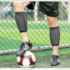 A person wearing black shorts and a white shirt is kneeling on a soccer field, demonstrating durable shin guards.