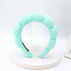 A light mint green sponge terry cloth headband for hair styling displayed on a white circular stand.