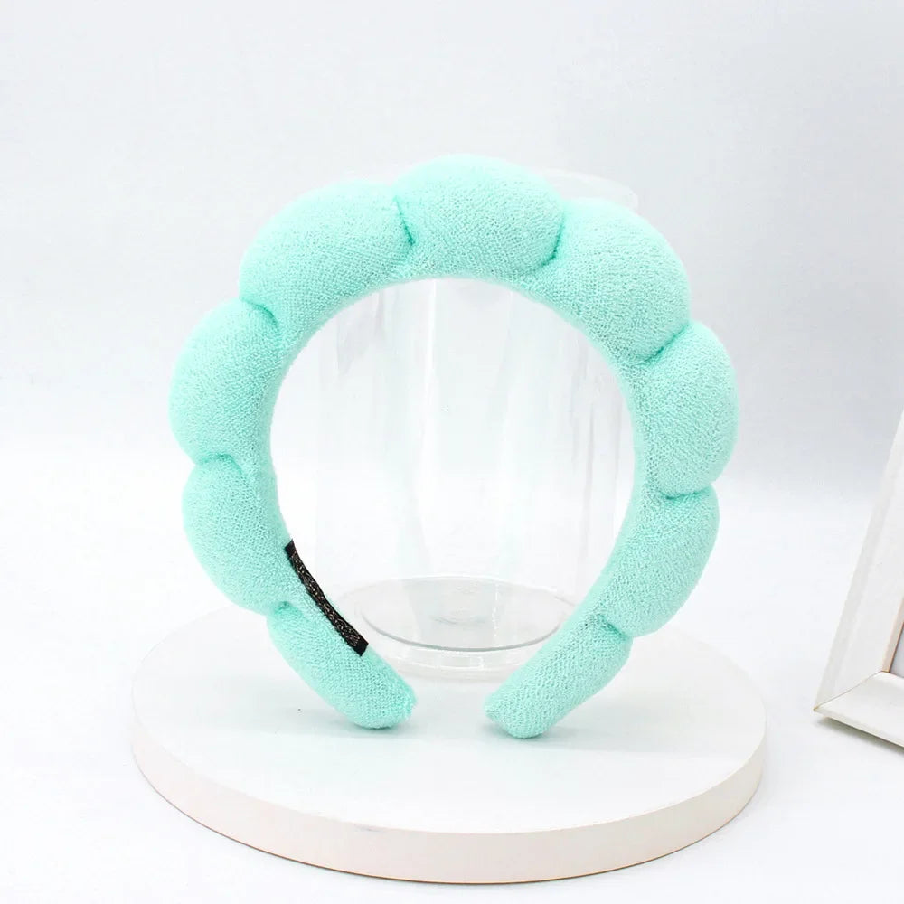 A light mint green sponge terry cloth headband for hair styling displayed on a white circular stand.