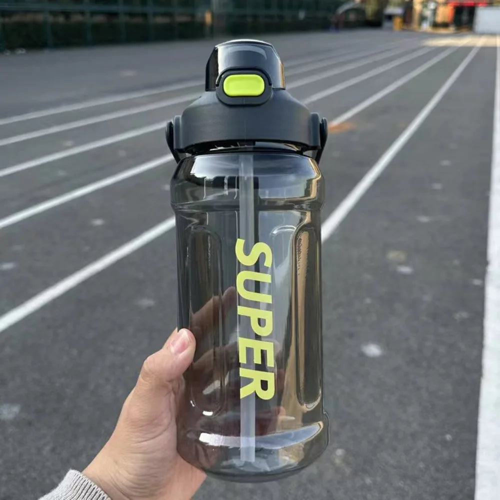 A hand holds a clear insulated sports water bottle with a black cap and yellow label against an asphalt background.