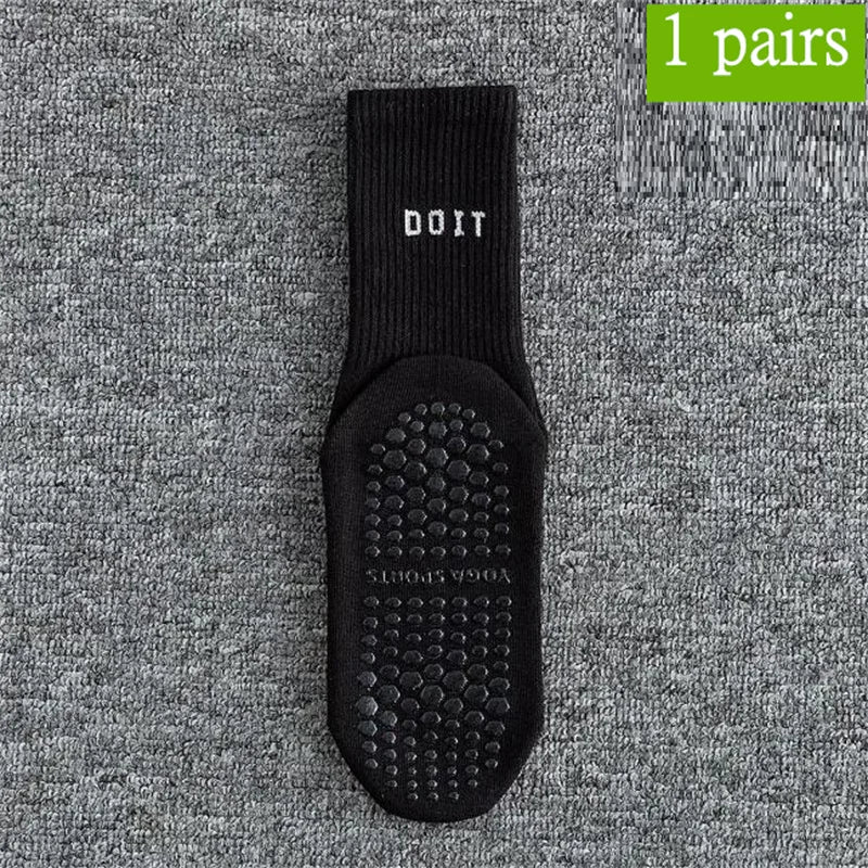 Ein Paar schwarze DOIT Yoga- und Fitnesssocken mit strukturierter Sohle auf grauem Stoff.