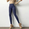 A person wearing dark navy high-waist seamless yoga leggings and a beige top standing against a white wall.
