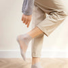 A person wearing sheer lace mesh ankle socks while standing on a wooden floor.