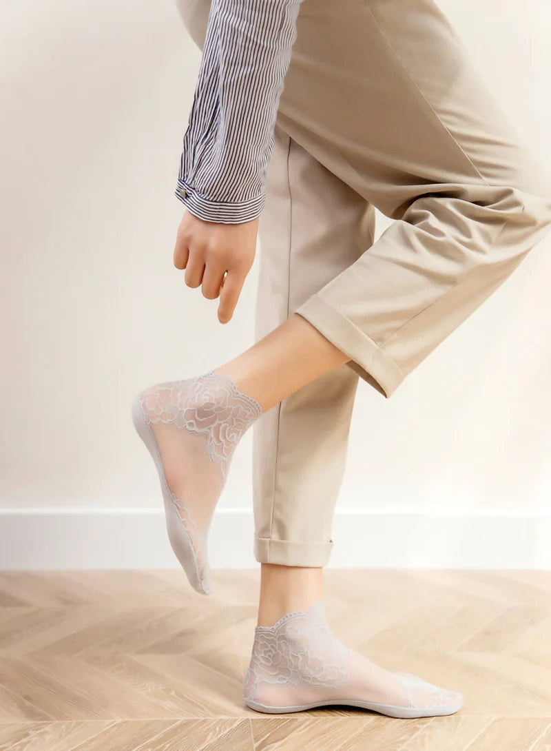 A person wearing sheer lace mesh ankle socks while standing on a wooden floor.