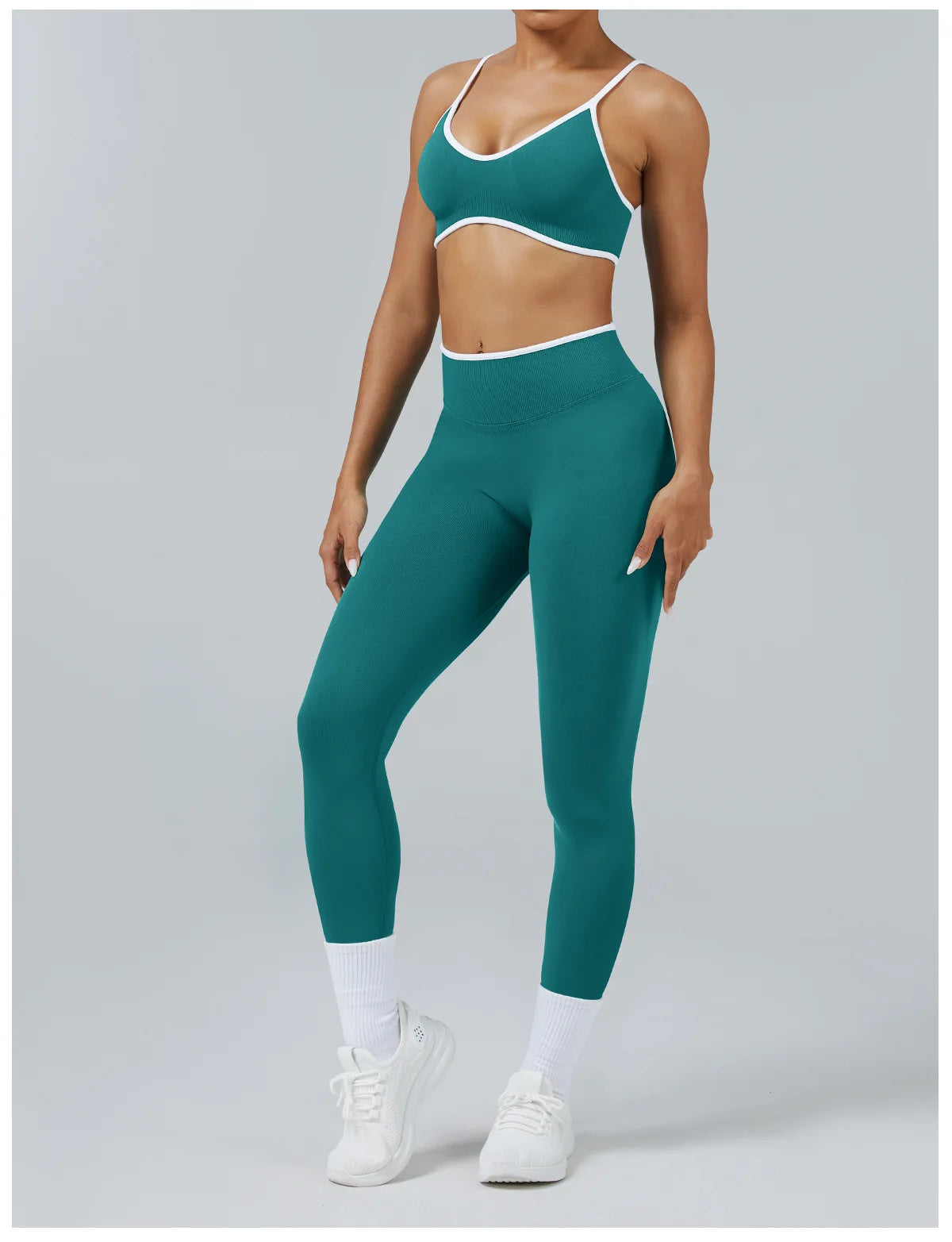 A woman wearing teal high-waist yoga leggings and a matching sports bra, standing against a light gray background.