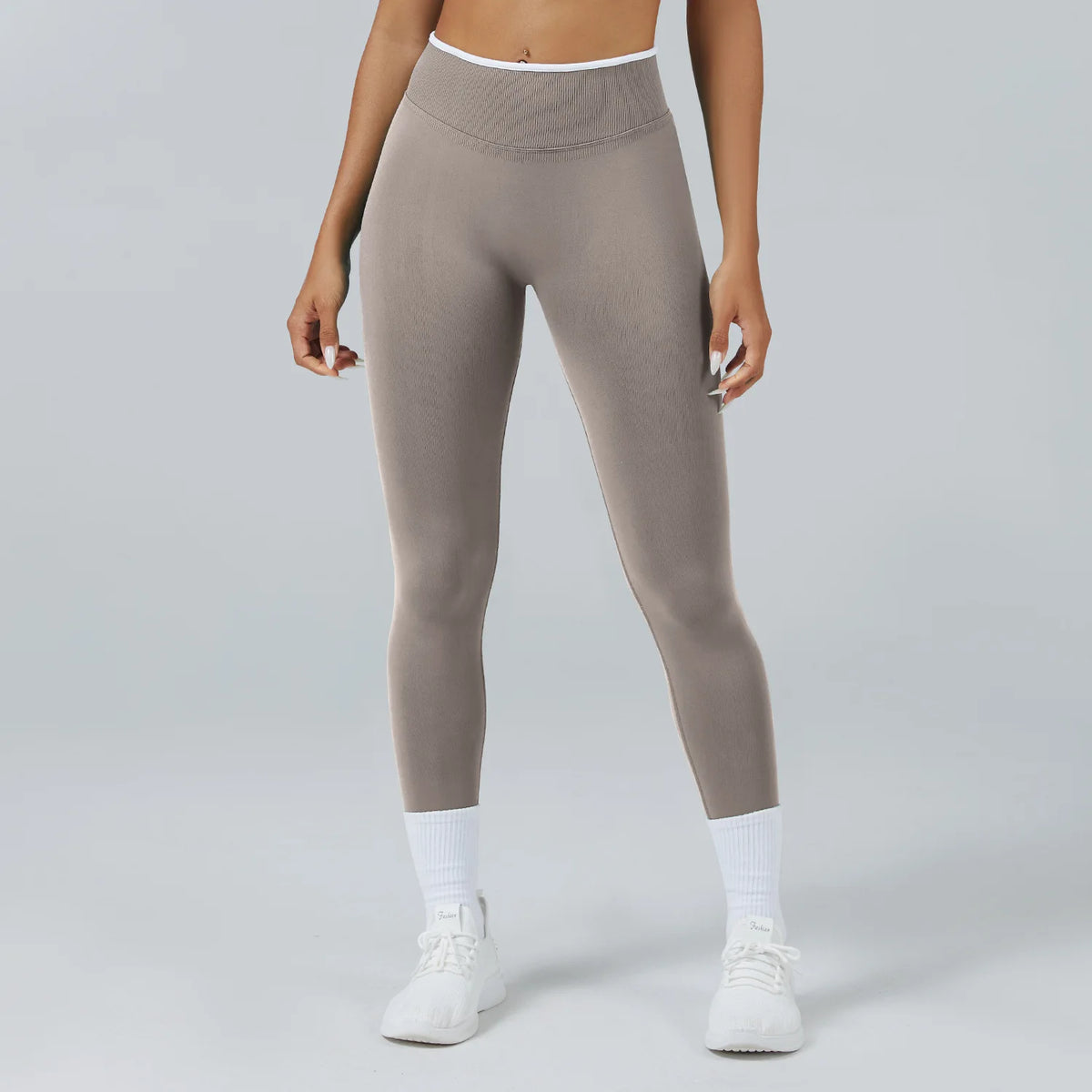 A person wearing high-waist grey yoga leggings and white socks standing against a light gray background.