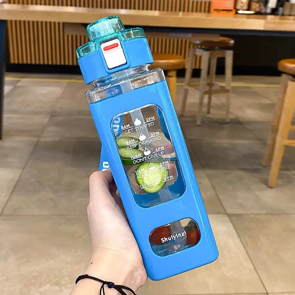 A hand holds a blue leakproof sport water bottle with time markings and a green liquid inside.