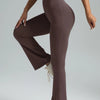 A model wearing high-waisted bootcut yoga pants and a purple top, standing in a side profile.