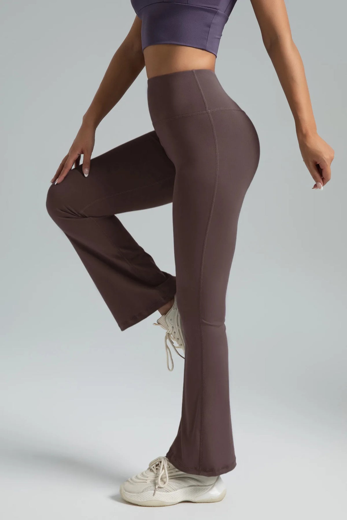 A model wearing high-waisted bootcut yoga pants and a purple top, standing in a side profile.
