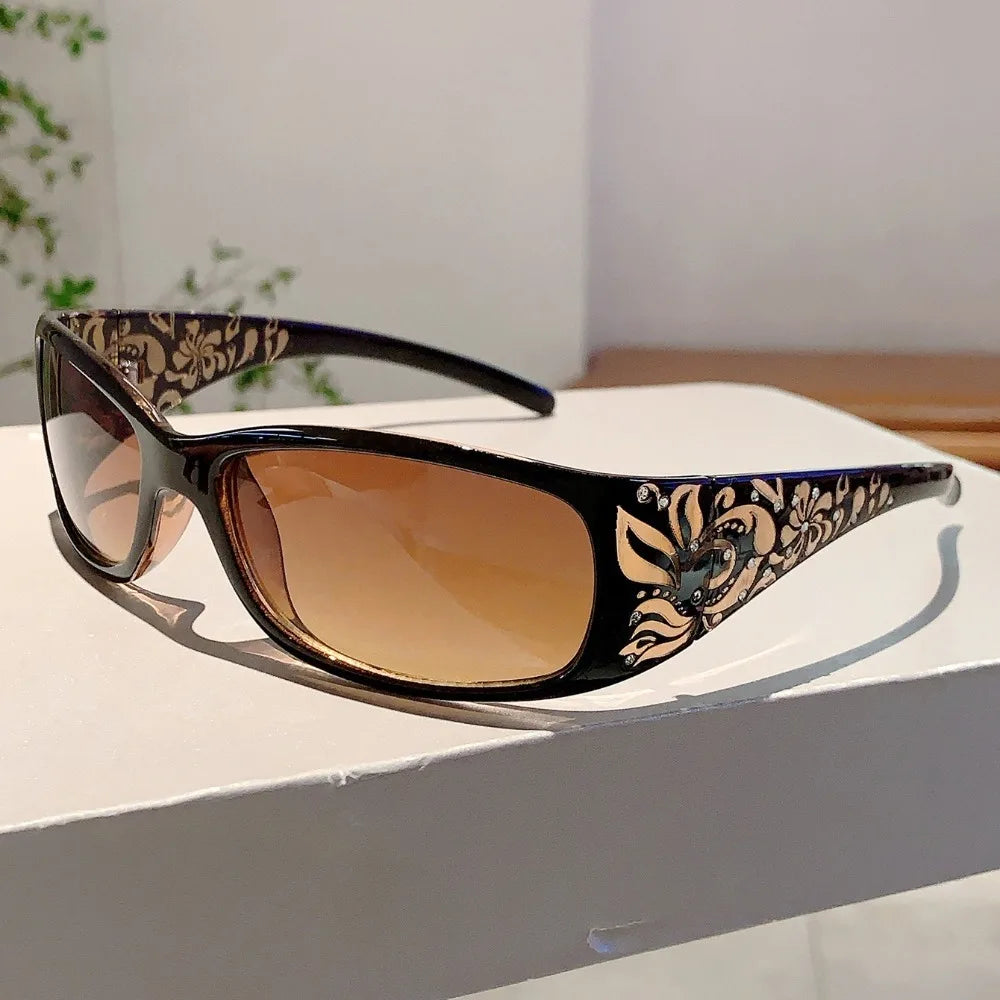 Brown tinted sunglasses with black frames featuring gold and floral rhinestone detailing.